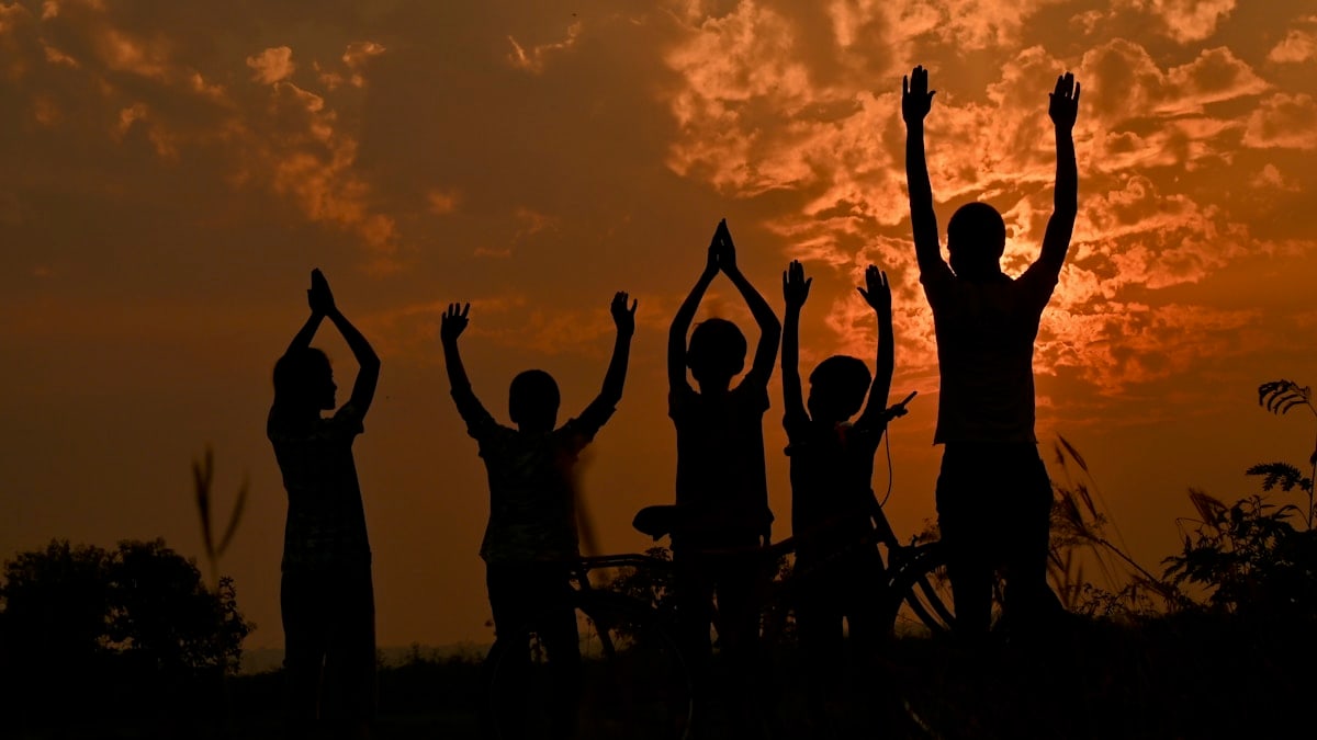 silhouette of people standing and raising their hands during sunset